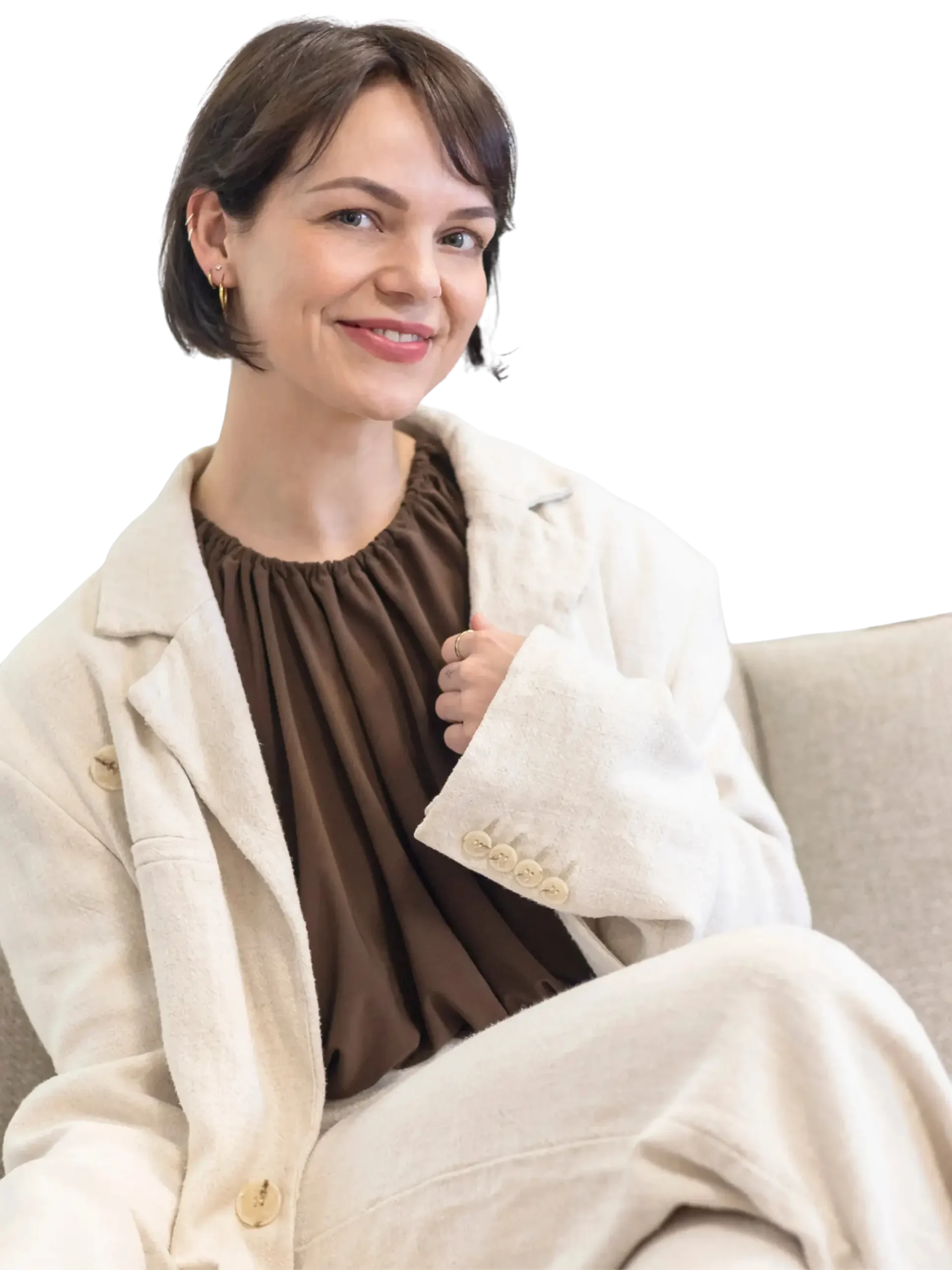 Glimlachende huidtherapeut van Huidskillskliniek met kort bruin haar, gekleed in een beige pak en bruine blouse, zittend tegen een donkere achtergrond.